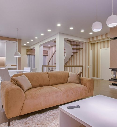 Luxurious living room with modern interior design, featuring beige sofa, fireplace, and open kitchen.